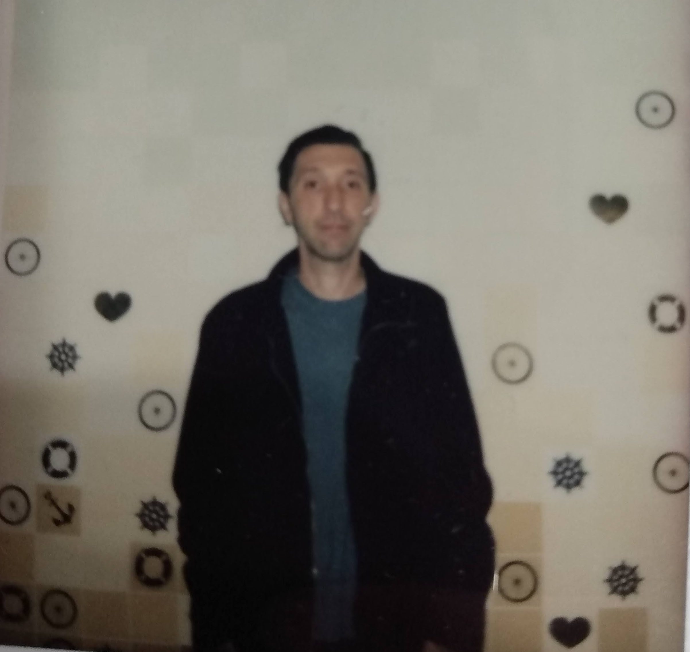 Joe Sullivan in a green shirt and black jacket in front of a wall with small stars and hearts